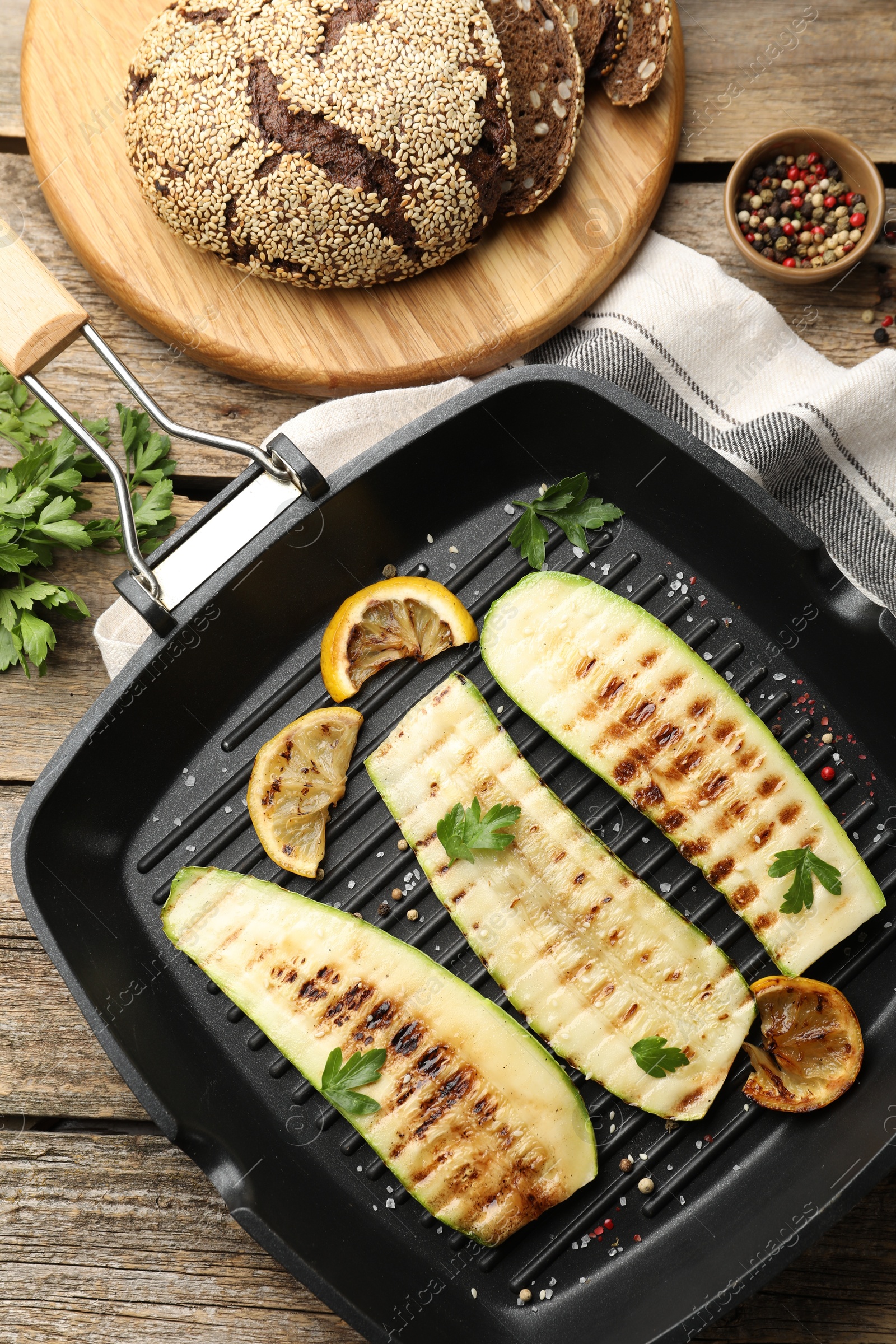 Photo of Delicious grilled courgette slices with spices and lemon in pan on wooden table, flat lay