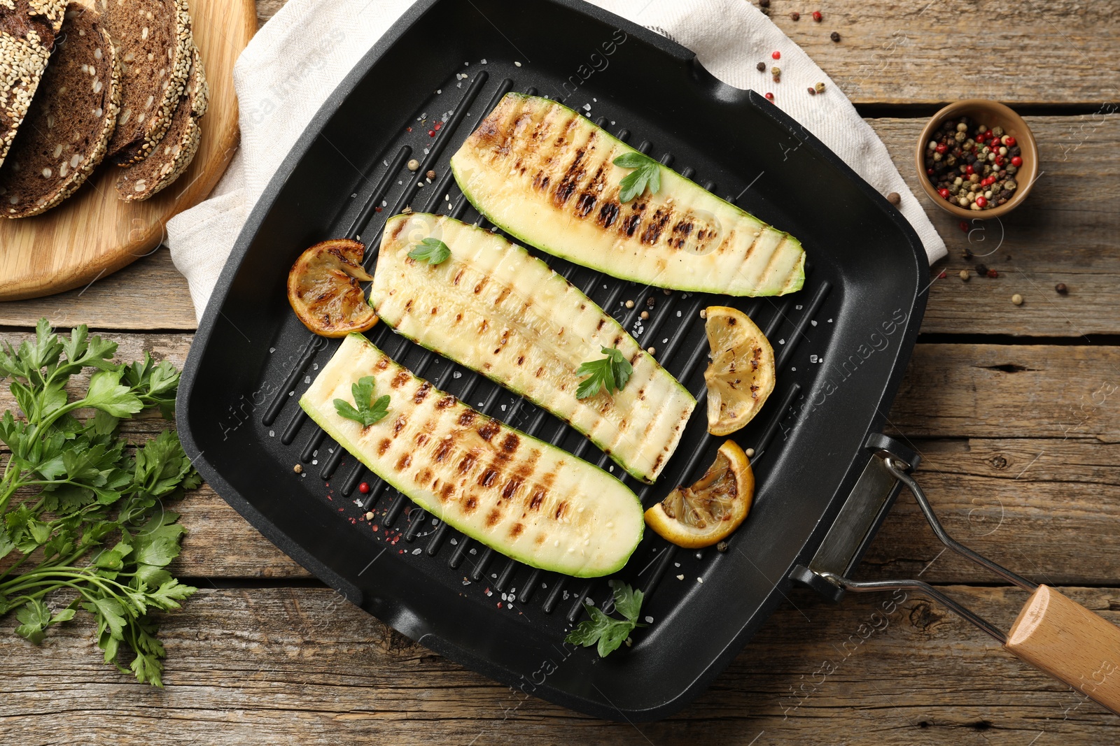 Photo of Delicious grilled courgette slices with spices and lemon in pan on wooden table, flat lay
