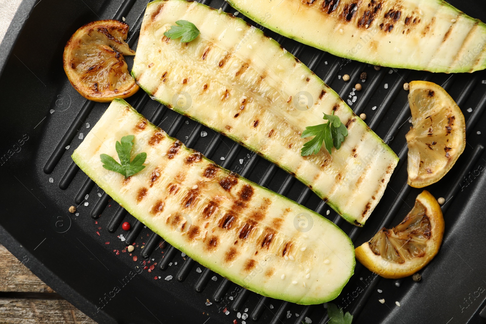 Photo of Delicious grilled courgette slices with spices and lemon in pan on table, top view
