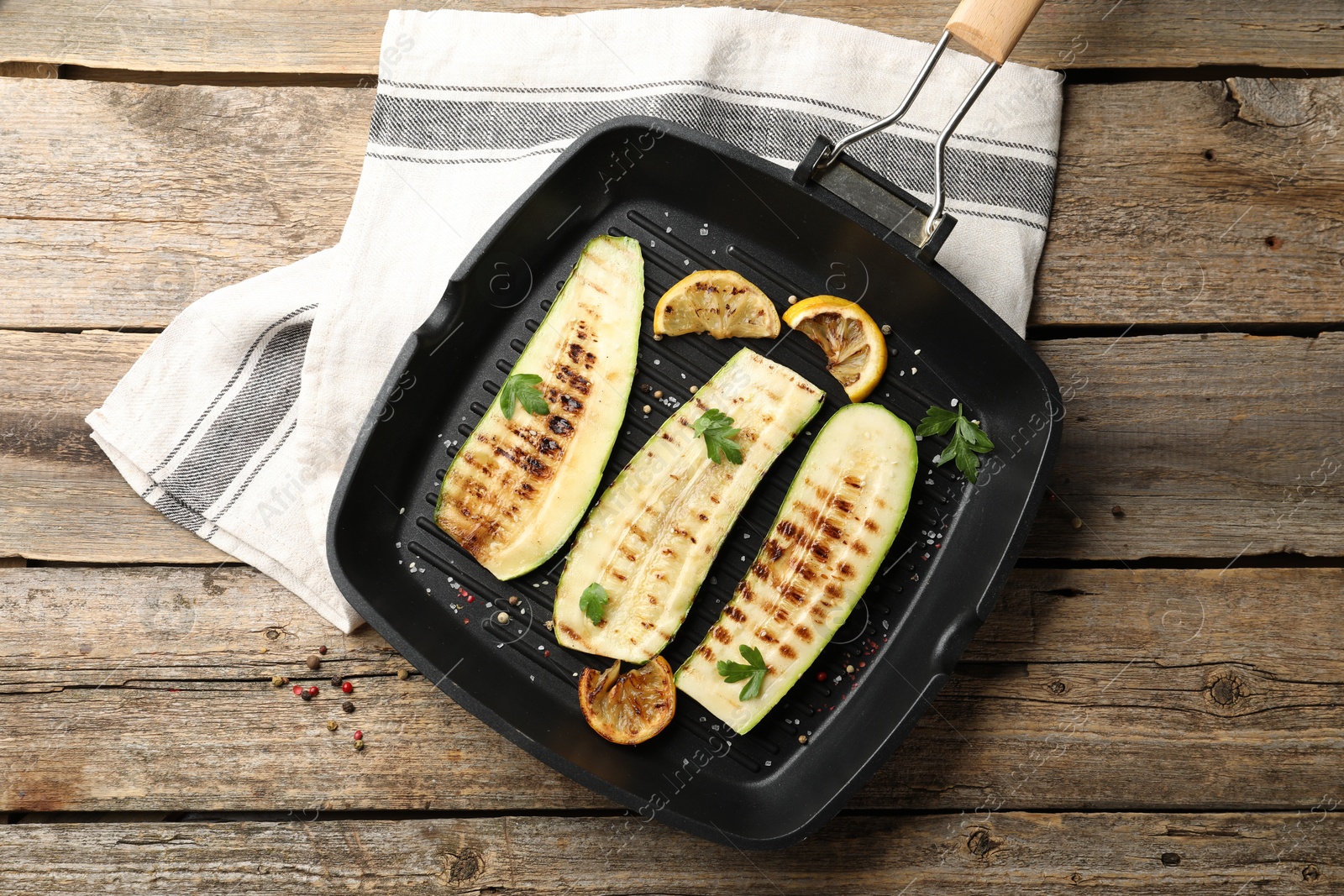 Photo of Delicious grilled courgette slices with spices and lemon in pan on wooden table, top view