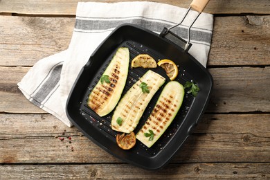Photo of Delicious grilled courgette slices with spices and lemon in pan on wooden table, top view