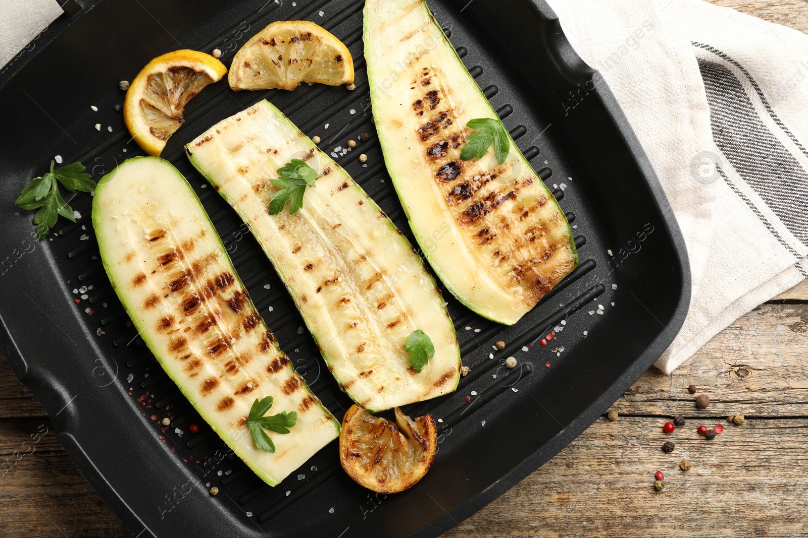 Photo of Delicious grilled courgette slices with spices and lemon in pan on wooden table, top view