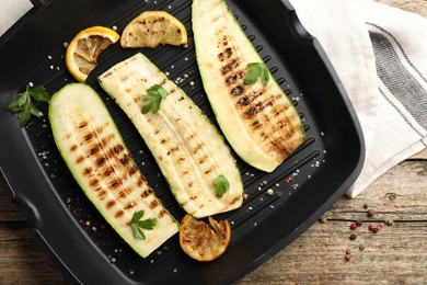 Photo of Delicious grilled courgette slices with spices and lemon in pan on wooden table, top view