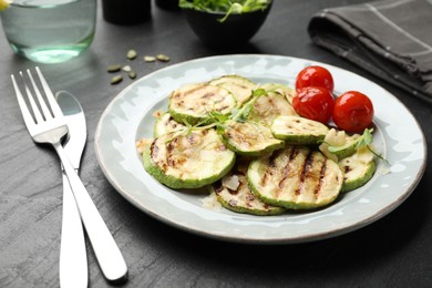 Photo of Delicious grilled courgette slices with tomatoes and microgreens served on black textured table, closeup