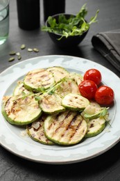 Photo of Delicious grilled courgette slices with tomatoes and microgreens on black table, closeup