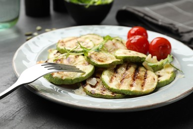 Photo of Delicious grilled courgette slices with tomatoes and microgreens served on black table, closeup