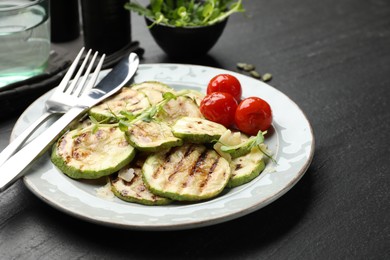 Photo of Delicious grilled courgette slices with tomatoes and microgreens served on black textured table, closeup