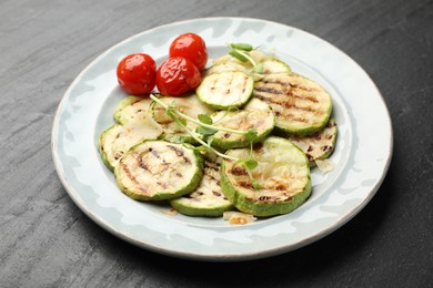 Photo of Delicious grilled courgette slices with tomatoes and microgreens on black textured table, closeup