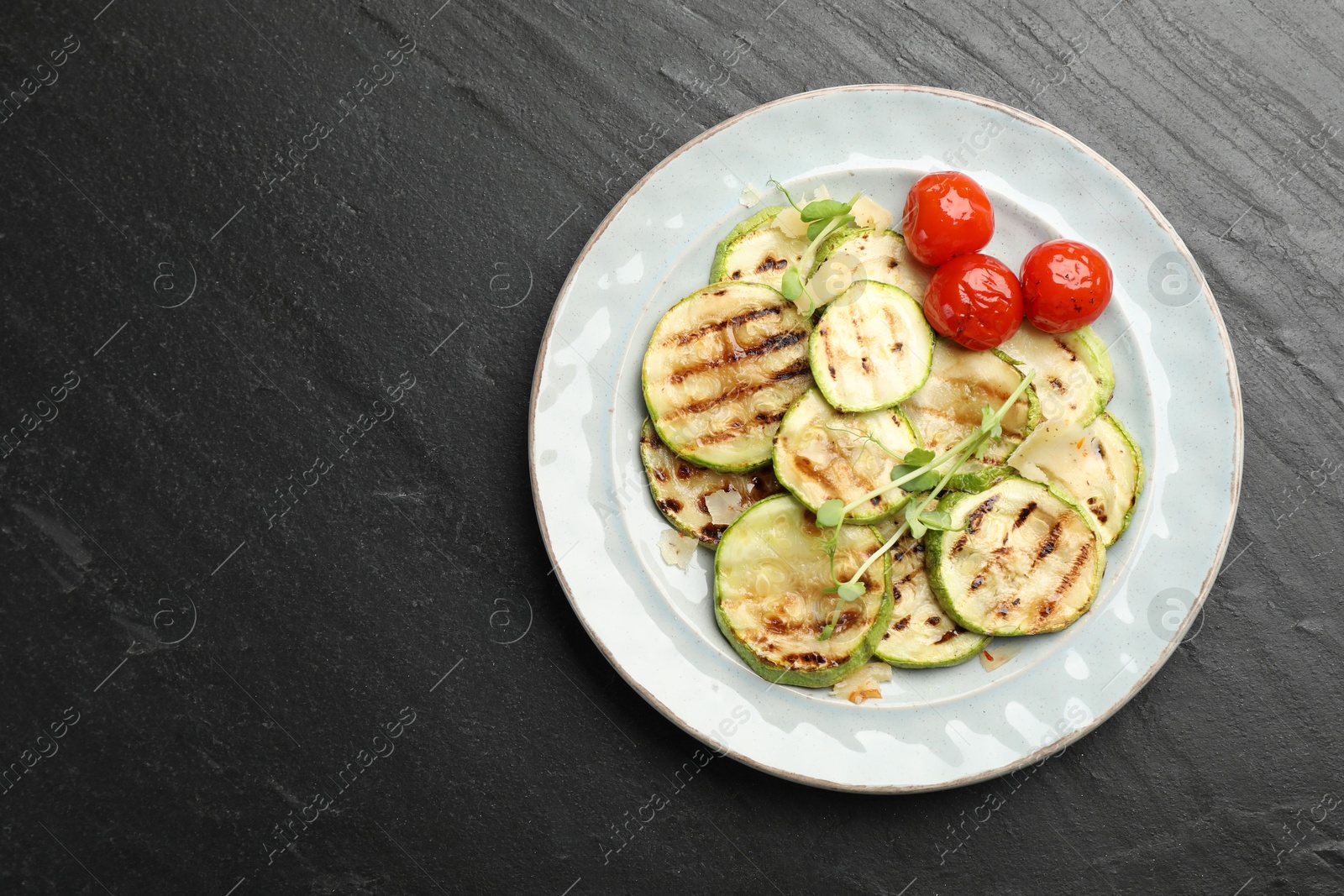 Photo of Delicious grilled courgette slices with tomatoes and microgreens on black textured table, top view. Space for text