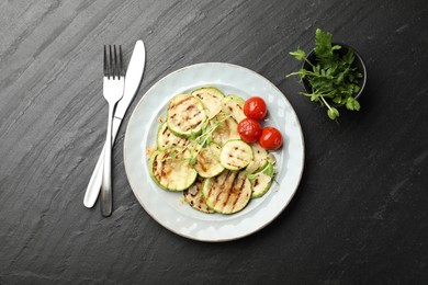 Photo of Delicious grilled courgette slices with tomatoes and microgreens served on black textured table, flat lay