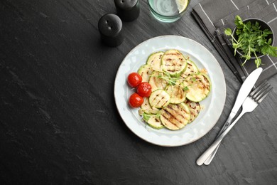 Photo of Delicious grilled courgette slices with tomatoes and microgreens served on black textured table, flat lay. Space for text