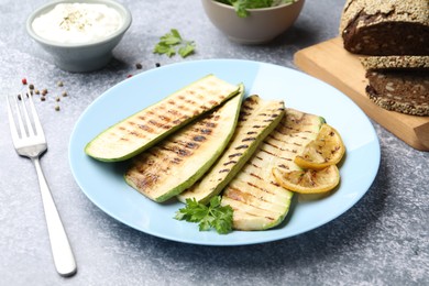 Photo of Delicious grilled courgette slices with parsley and lemon served on gray textured table, closeup