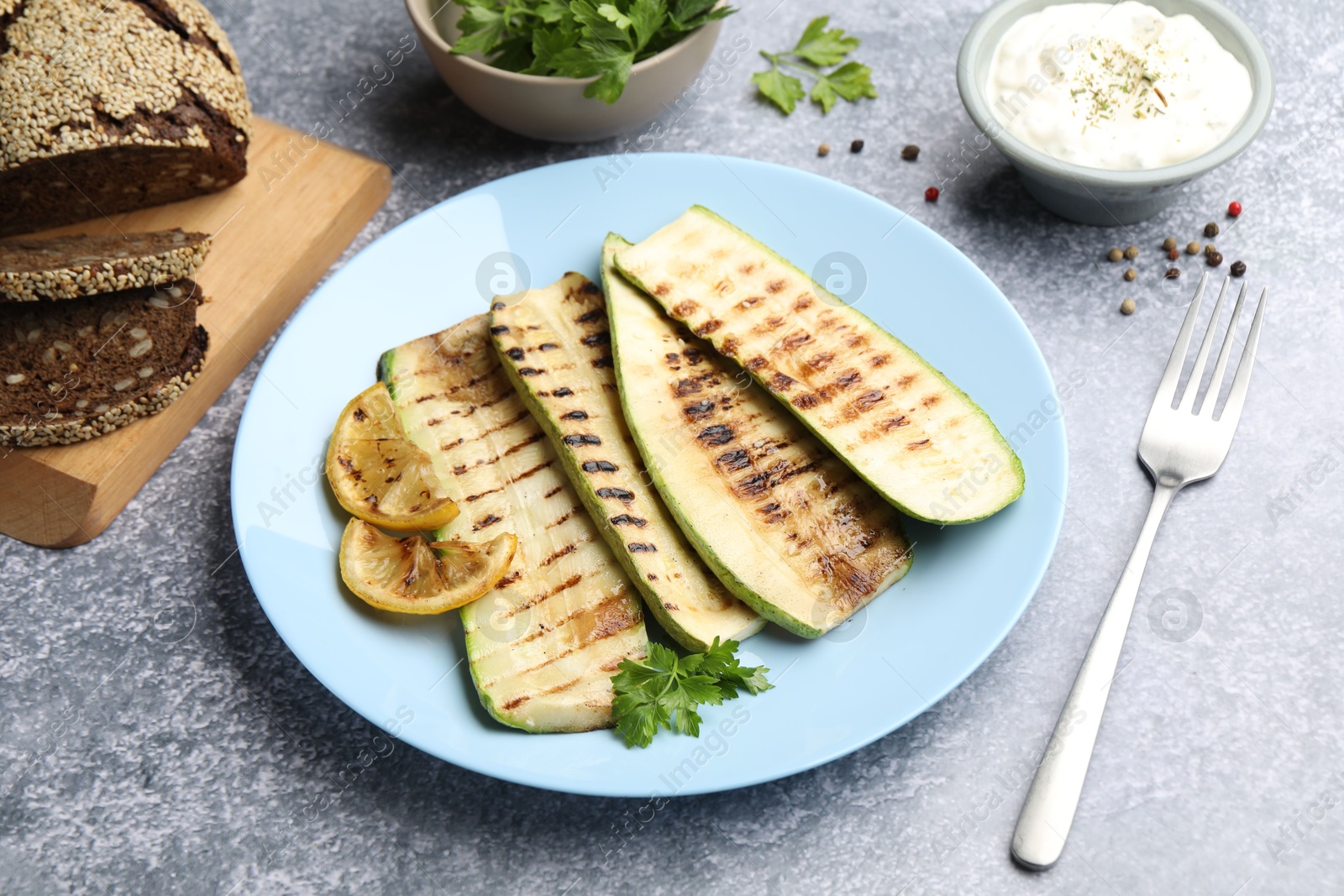 Photo of Delicious grilled courgette slices with parsley and lemon served on gray textured table, closeup