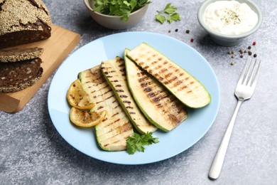 Photo of Delicious grilled courgette slices with parsley and lemon served on gray textured table, closeup