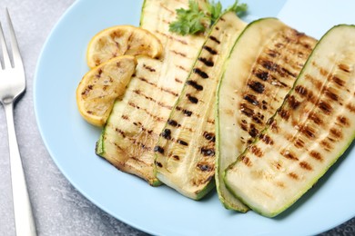 Photo of Delicious grilled courgette slices with parsley and lemon served on gray table, closeup