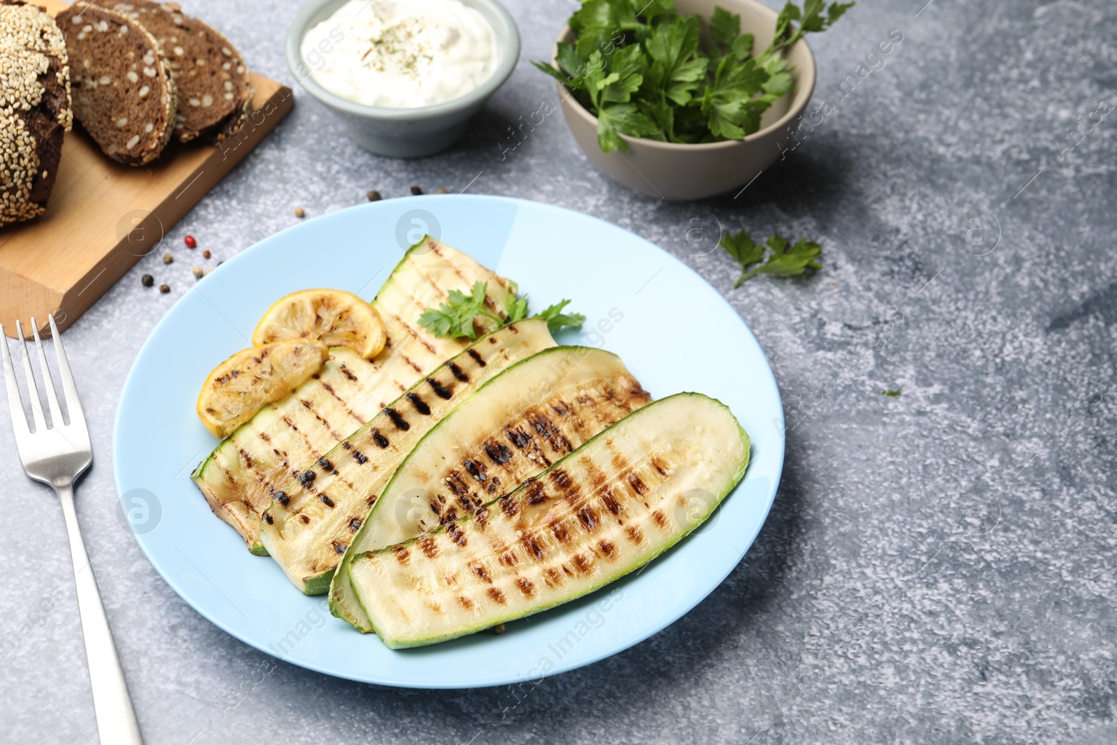 Photo of Delicious grilled courgette slices with parsley and lemon served on gray textured table, closeup