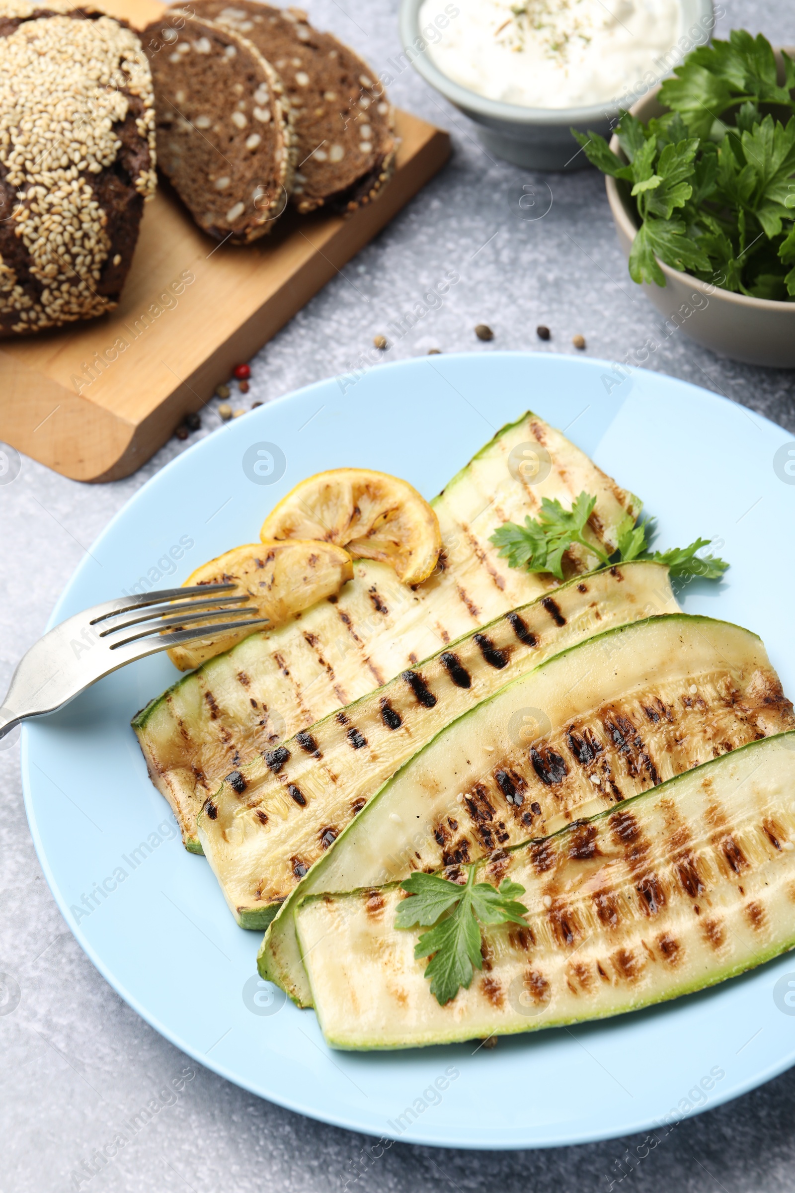 Photo of Delicious grilled courgette slices with parsley and lemon served on gray textured table, closeup
