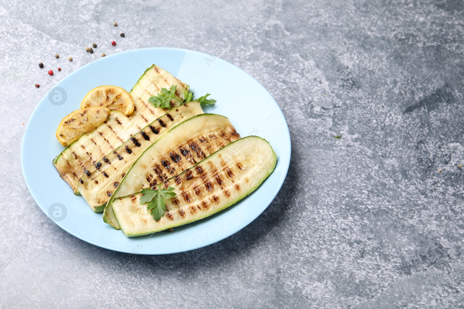 Photo of Delicious grilled courgette slices with parsley and lemon on gray textured table, closeup. Space for text