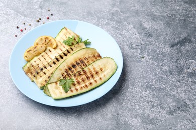 Photo of Delicious grilled courgette slices with parsley and lemon on gray textured table, closeup. Space for text