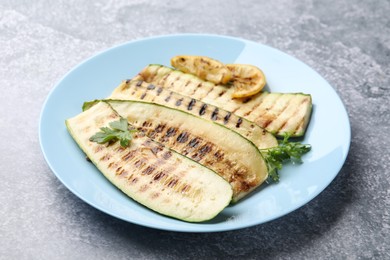 Photo of Delicious grilled courgette slices with parsley and lemon on gray textured table, closeup