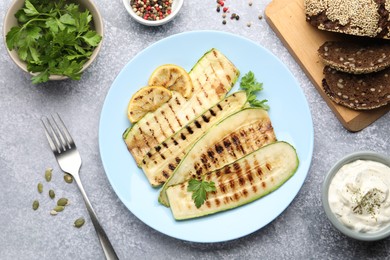 Photo of Delicious grilled courgette slices with parsley and lemon served on gray textured table, flat lay