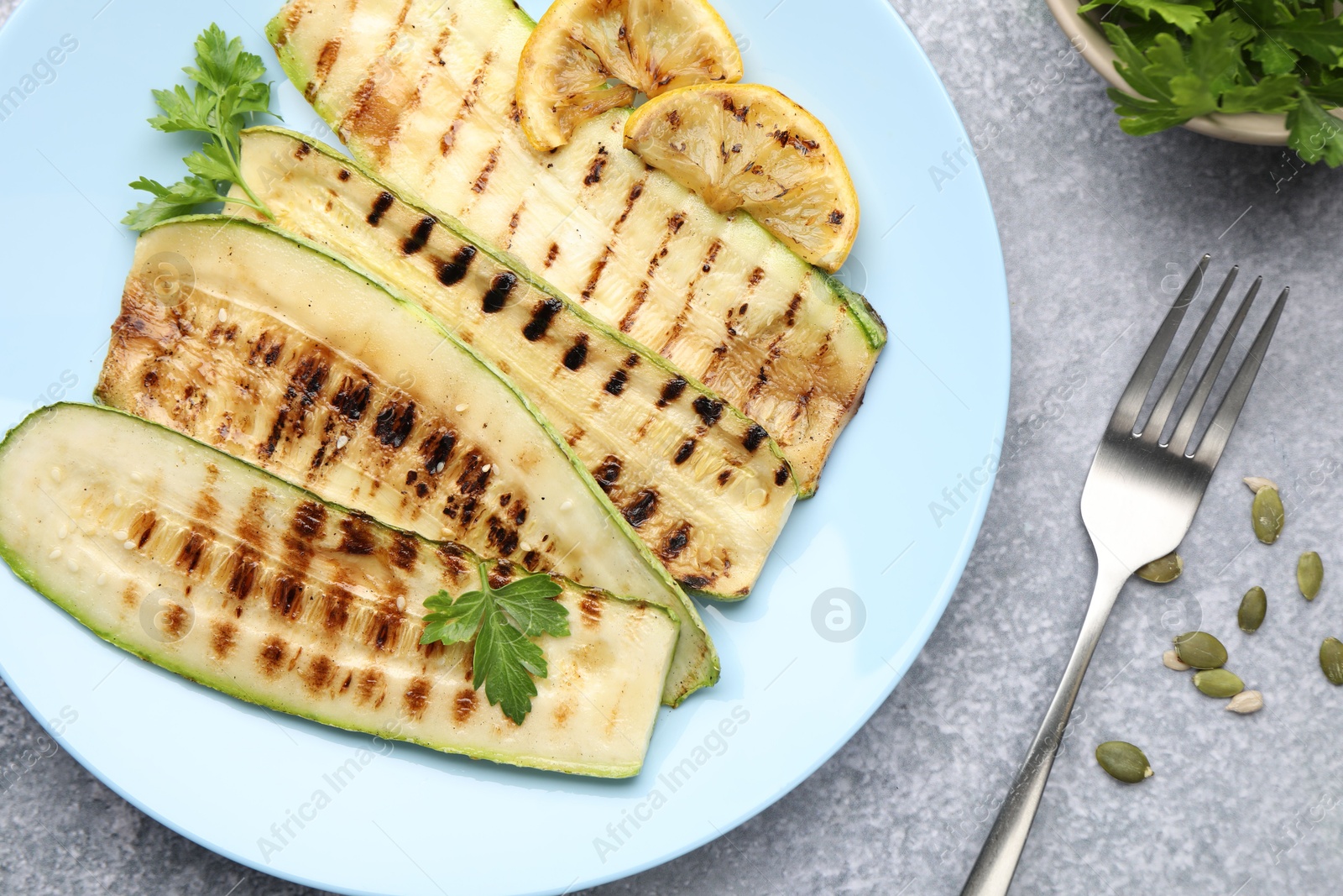 Delicious grilled courgette slices with parsley and lemon served on gray textured table, flat lay Photo of Delicious grilled courgette slices with parsley and lemon served on gray textured table, flat lay