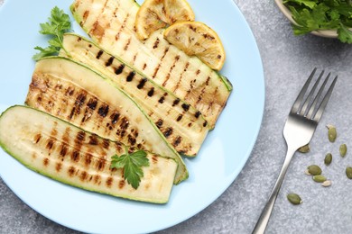 Photo of Delicious grilled courgette slices with parsley and lemon served on gray textured table, flat lay