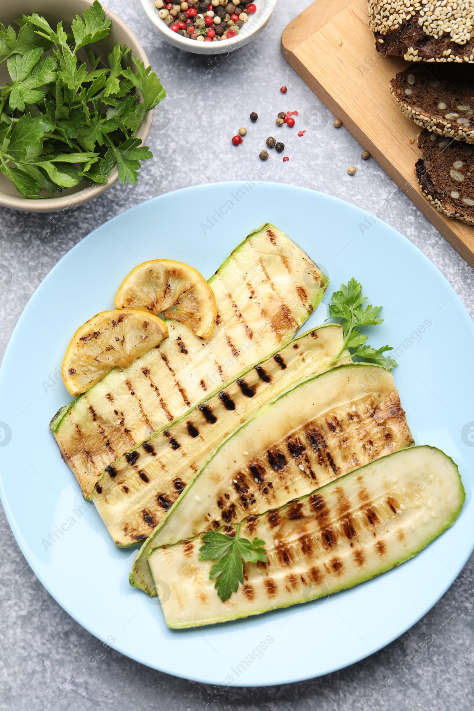 Delicious grilled courgette slices with spices, lemon and bread on gray textured table, flat lay Photo of Delicious grilled courgette slices with spices, lemon and bread on gray textured table, flat lay