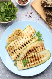 Photo of Delicious grilled courgette slices with spices, lemon and bread on gray textured table, flat lay