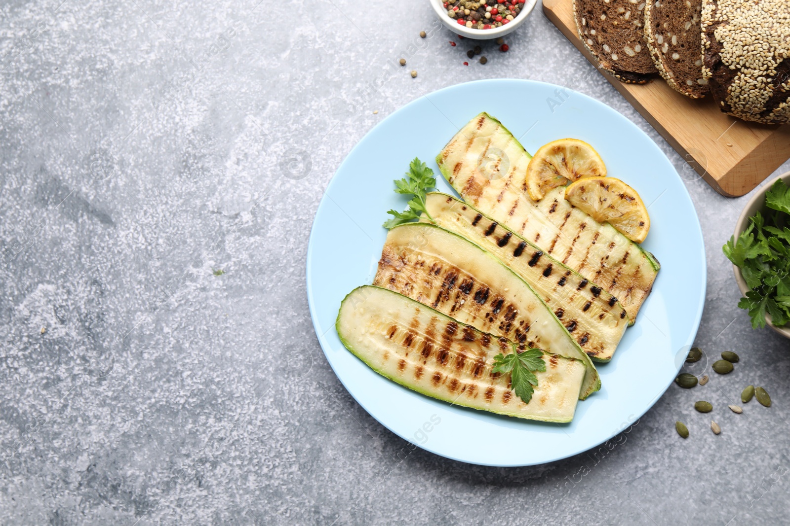 Delicious grilled courgette slices with spices, lemon and bread on gray textured table, flat lay. Space for text Photo of Delicious grilled courgette slices with spices, lemon and bread on gray textured table, flat lay. Space for text