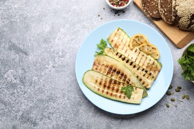 Photo of Delicious grilled courgette slices with spices, lemon and bread on gray textured table, flat lay. Space for text