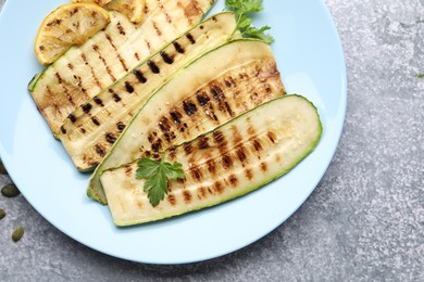 Photo of Delicious grilled courgette slices with parsley and lemon on gray textured table, flat lay
