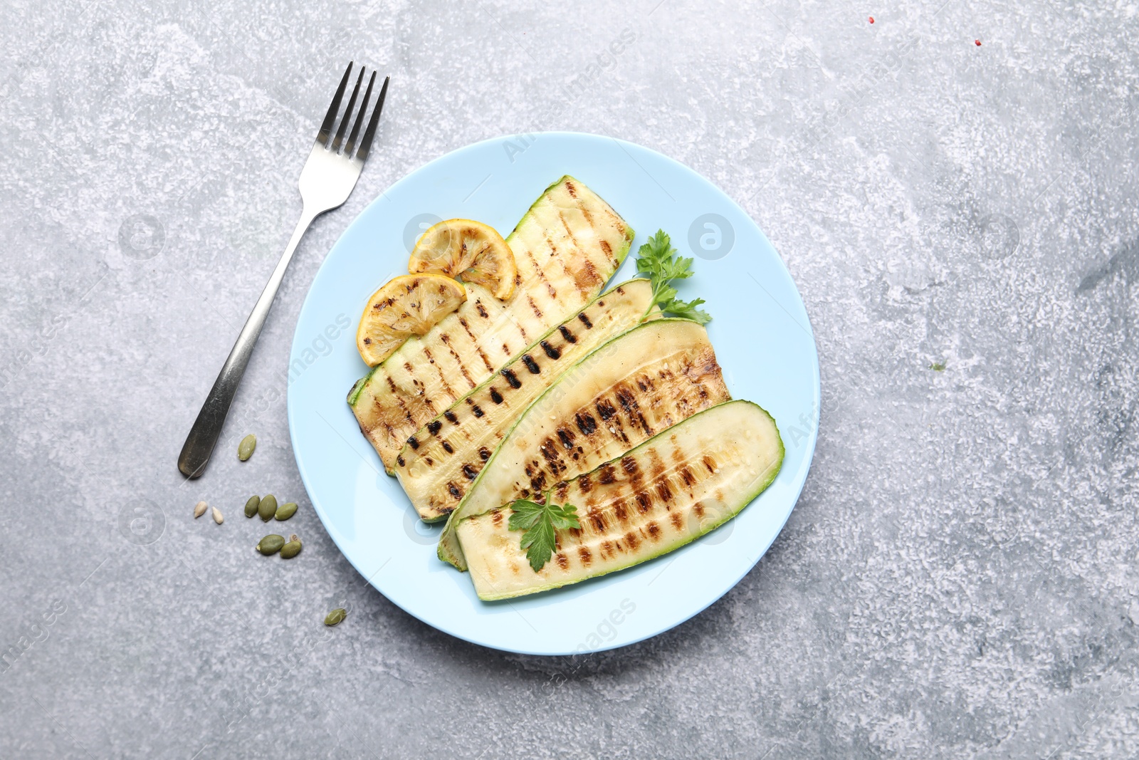 Delicious grilled courgette slices with parsley and lemon served on gray textured table, flat lay Photo of Delicious grilled courgette slices with parsley and lemon served on gray textured table, flat lay