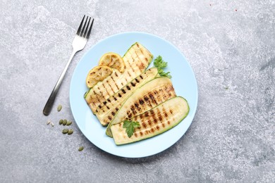 Photo of Delicious grilled courgette slices with parsley and lemon served on gray textured table, flat lay