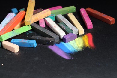 Photo of Many colorful chalk pastels on black background