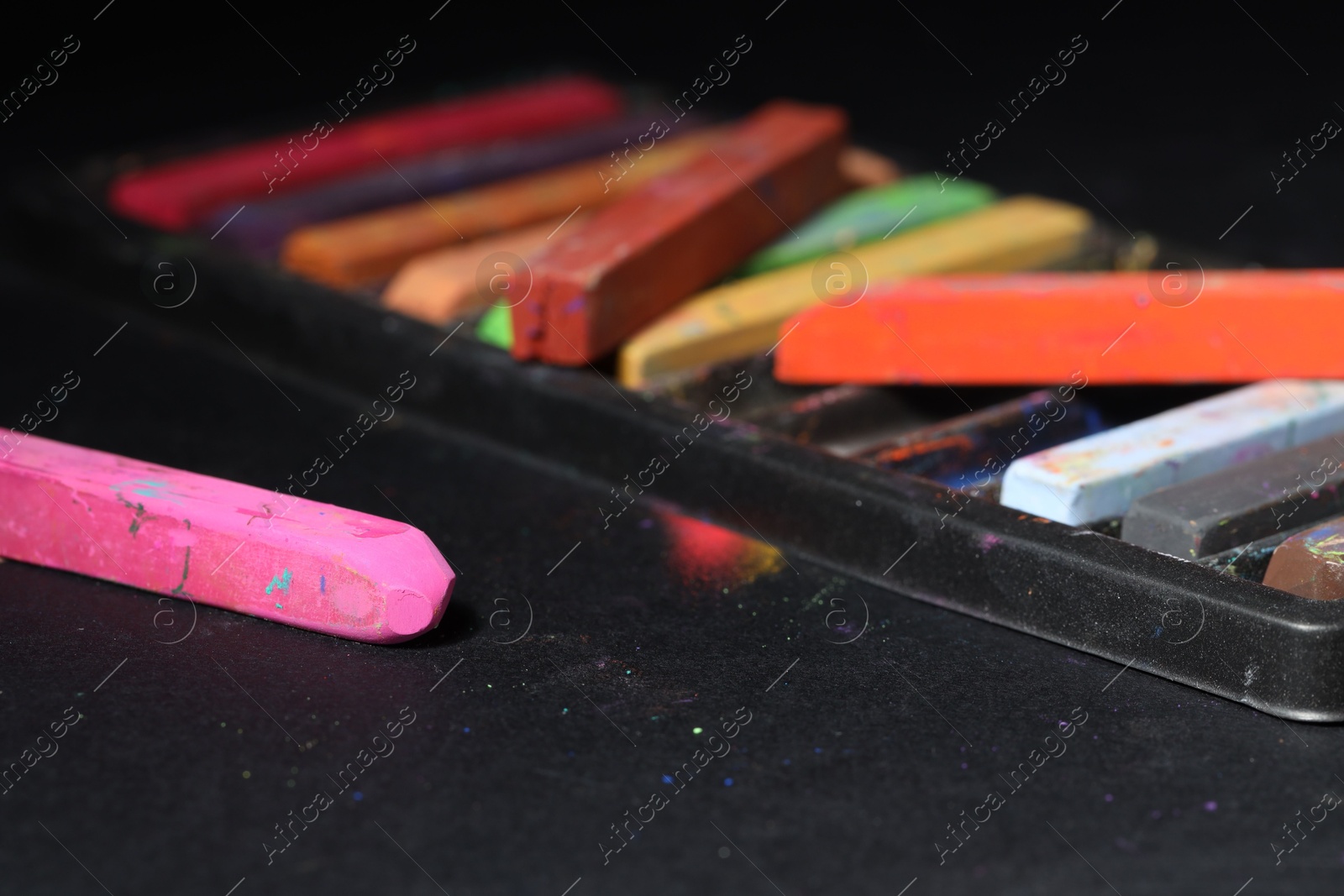 Photo of Colorful chalk pastels on black background, closeup
