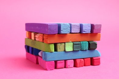 Photo of Many colorful chalk pastels on pink background, closeup