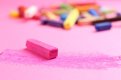 Photo of Many colorful chalk pastels on pink background, closeup