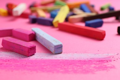 Photo of Many colorful chalk pastels on pink background, closeup