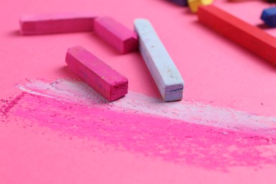 Photo of Many colorful chalk pastels on pink background, closeup