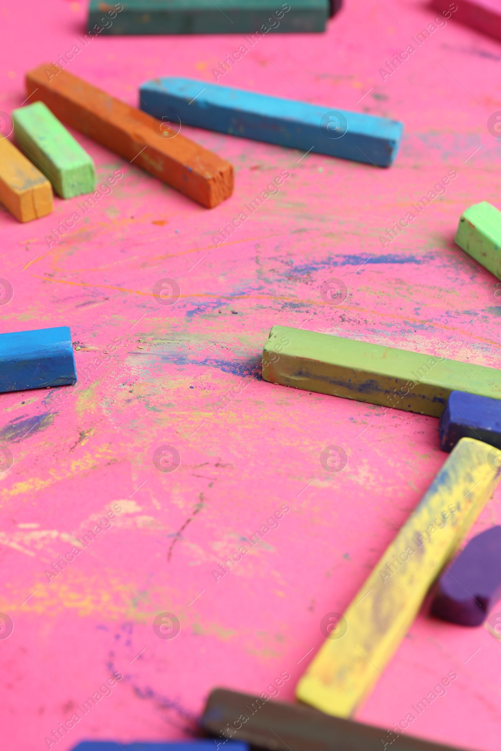 Photo of Many colorful chalk pastels on pink background, closeup