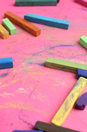 Photo of Many colorful chalk pastels on pink background, closeup