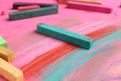 Photo of Many colorful chalk pastels on pink background, closeup