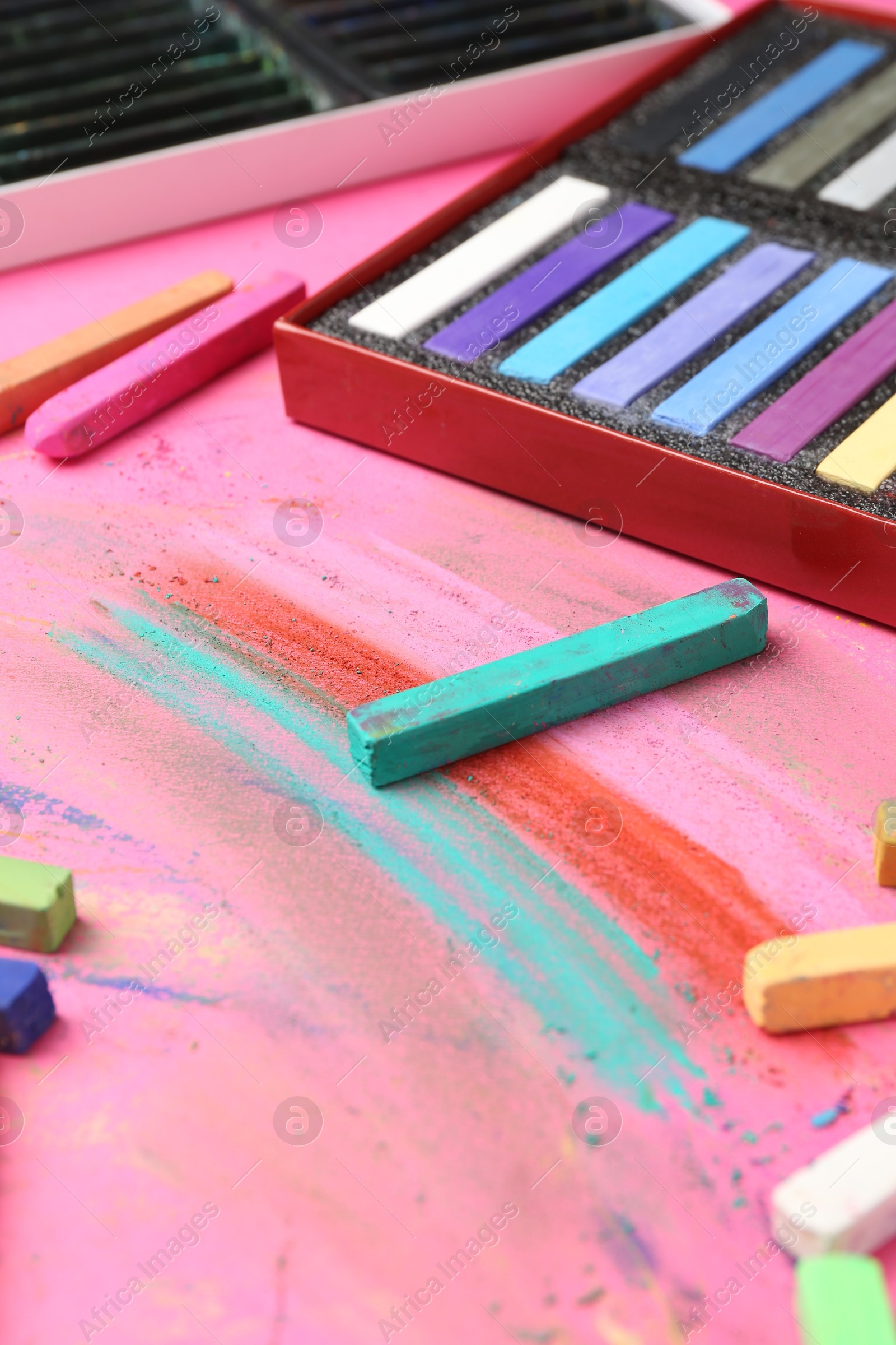Photo of Many colorful chalk pastels on pink background, closeup