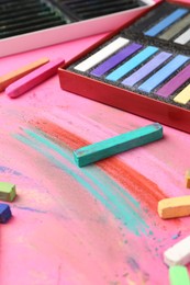 Photo of Many colorful chalk pastels on pink background, closeup