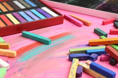 Photo of Many colorful chalk pastels on pink background, closeup