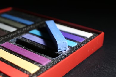 Photo of Many colorful chalk pastels on black background, closeup