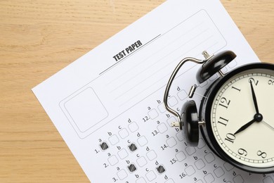 Photo of Answer sheet and alarm clock on wooden table, flat lay. Student passing exam