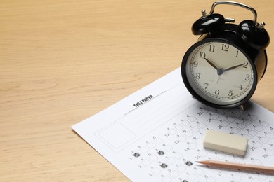 Photo of Answer sheet, eraser, pencil and alarm clock on wooden table, closeup. Student passing exam