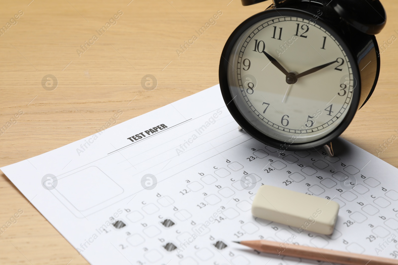 Photo of Answer sheet, eraser, pencil and alarm clock on wooden table, closeup. Student passing exam